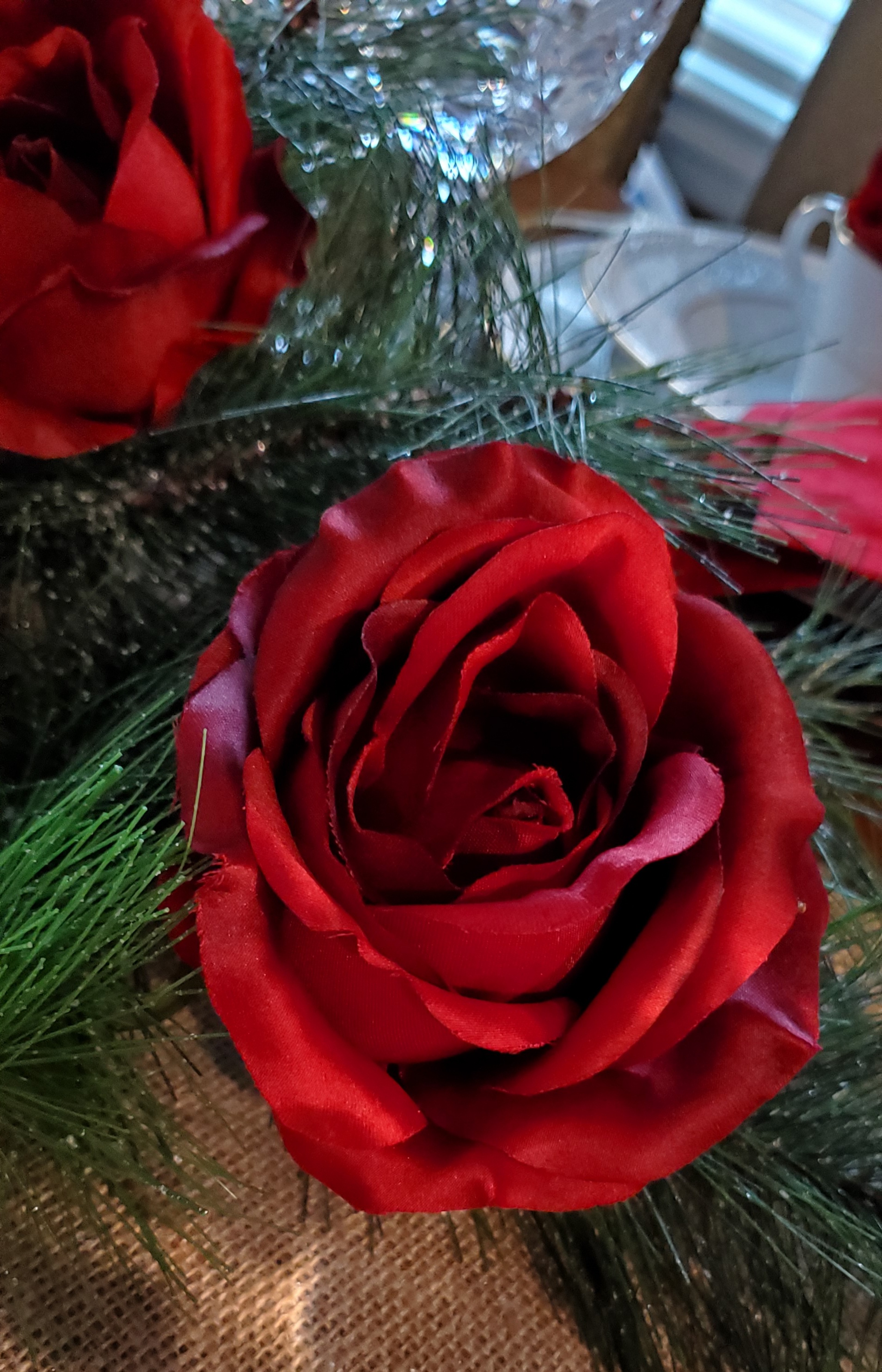 Two silk red roses in garland on a dining room table runner